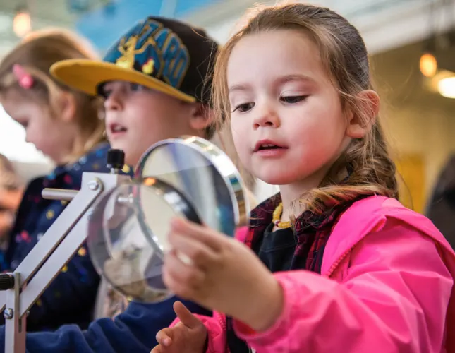 Young children exploring a hands-on interactive science exhibit, handling equipment and engaged in learning activities.