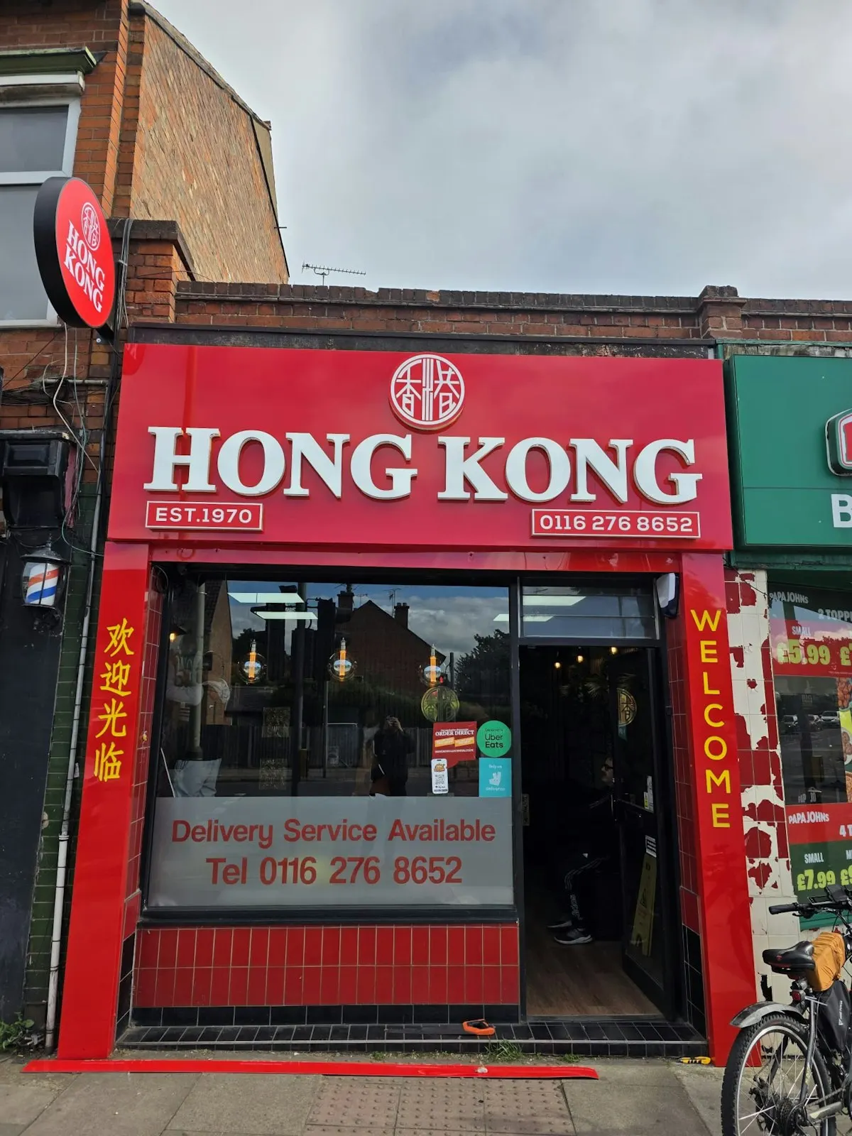 Red storefront of Hong Kong restaurant established 1970, with open entrance and bicycle parked outside.