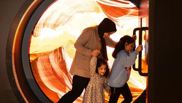Family of four exploring an interactive illuminated tunnel exhibit with glowing orange and white light patterns.