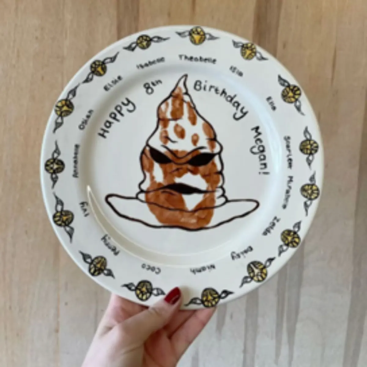 Person holding a decorative ceramic plate with a brown and white ice cream cone illustration and "Happy 8th Birthday" text.