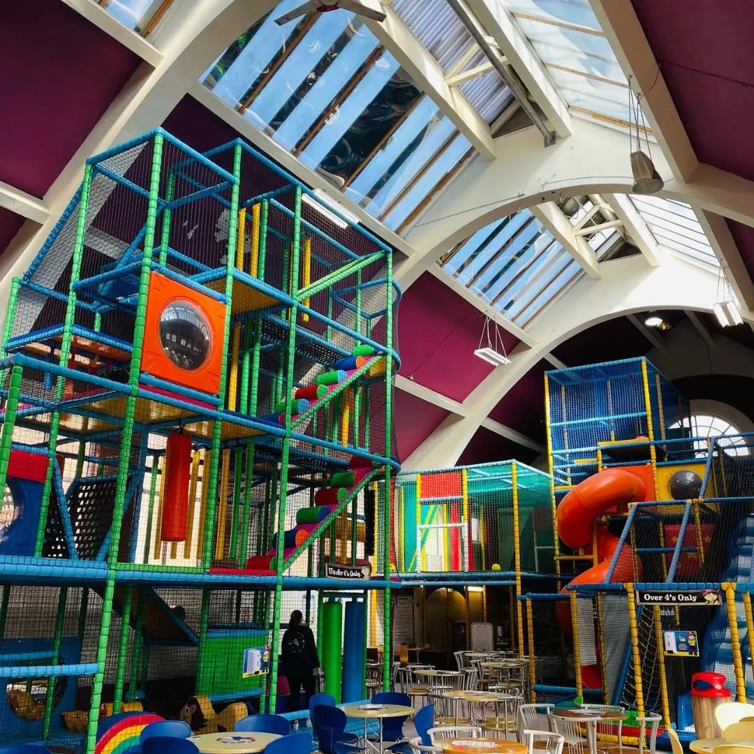 Wide view of under-4s and over-4s soft-play frames with cafe seating under vaulted ceiling